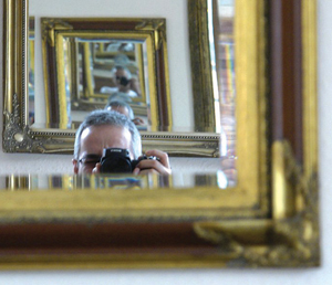 A man behind a camera, taking a photo of himself in a mirror, with multiple reflections